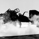 Black-and-white photo of steam rising around two or three grounded black planes, obscuring them.